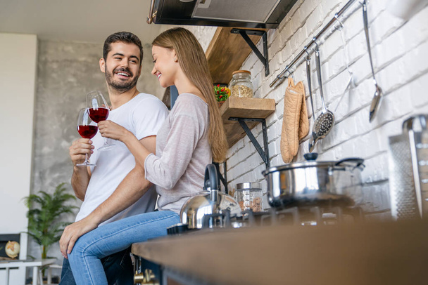 Young caucasian man and woman in love with wine glasses together in home kitchen - Foto, imagen