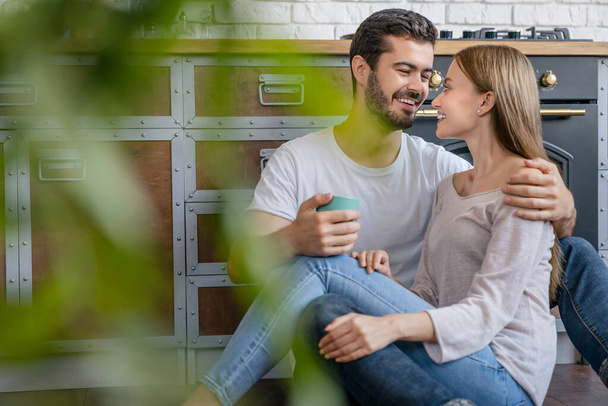 Happy young couple in love relaxing and hugging in kitchen having coffee on floor - Photo, image
