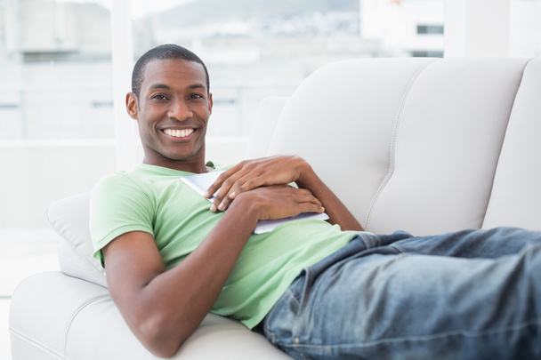 Casual smiling Afro man with digital tablet lying on sofa - Foto, Imagen