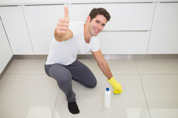 Man cleaning the kitchen floor while gesturing thumbs up - Photo, image