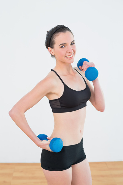 Smiling woman with dumbbells at fitness studio - Foto, afbeelding