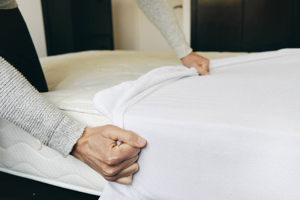 closeup of a young caucasian man covering a mattress with a white mattress protector - Foto, immagini