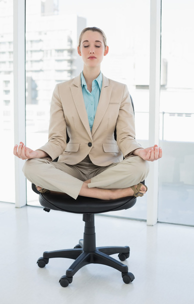 schöne elegante Geschäftsfrau meditiert in Lotusposition auf ihrem Drehstuhl - Foto, Bild