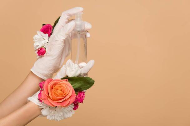 Ausgeschnittene Ansicht einer Frau in floralen Latex-Handschuhen mit antiseptischem Spray isoliert auf beige - Foto, Bild