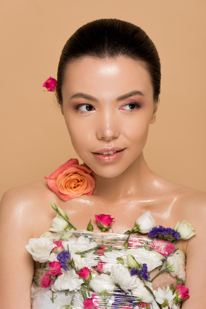 attractive naked asian girl in fresh flowers isolated on beige - Фото, зображення