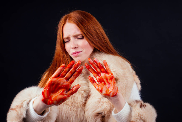 sad redhaired ginger fashion victim woman with blood on her hands wearing natural fur coat and crying,studio black background.stop animal killing please - Foto, Imagen
