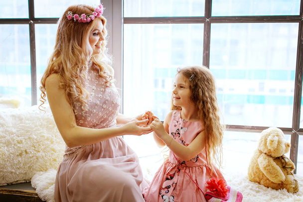 Beautiful mother and daughter talk and play by the window - Фото, изображение