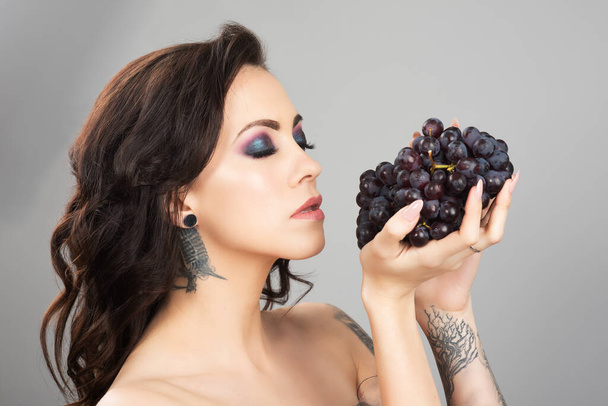 Woman with closed eyes holding blue grapes in front of her face. Eye shadows matching the color of the fruit. - Valokuva, kuva