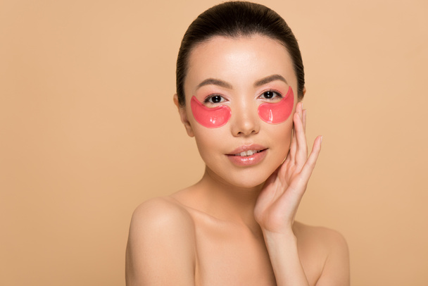 attractive tender naked asian woman with pink collagen eye pads isolated on beige - Fotó, kép