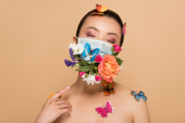 beautiful tender naked asian girl with closed eyes in floral face mask with butterflies isolated on beige - Zdjęcie, obraz