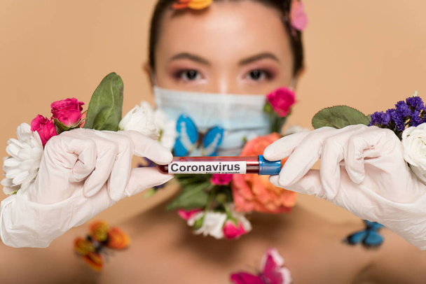 Çiçek maskeli çekici Asyalı kızın seçici odak noktası ve bej rengi üzerinde koronavirüs kan testi tutan lateks eldivenler. - Fotoğraf, Görsel