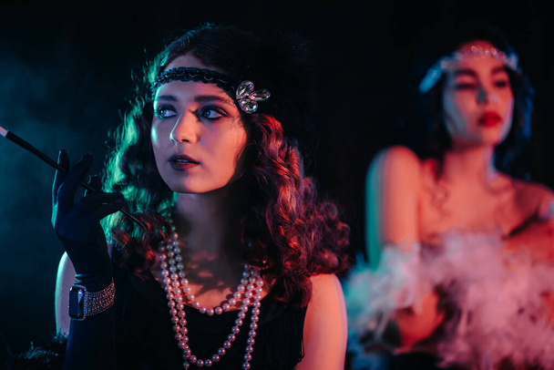 Attractive flappers women dressed in style of Roaring twenties posing on neon smoky background. Vintage, retro party, fashion, girls friends concept - Фото, зображення