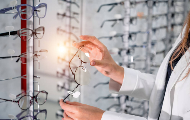 Showcase with spectacles in modern ophthalmic store. Hands with glasses. Closeup. - Fotoğraf, Görsel