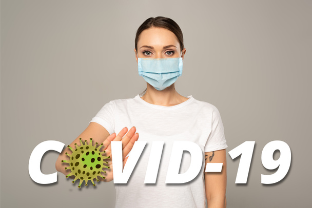 Woman in medical mask showing stop gesture isolated on grey, covid-19 illustration  - Photo, Image