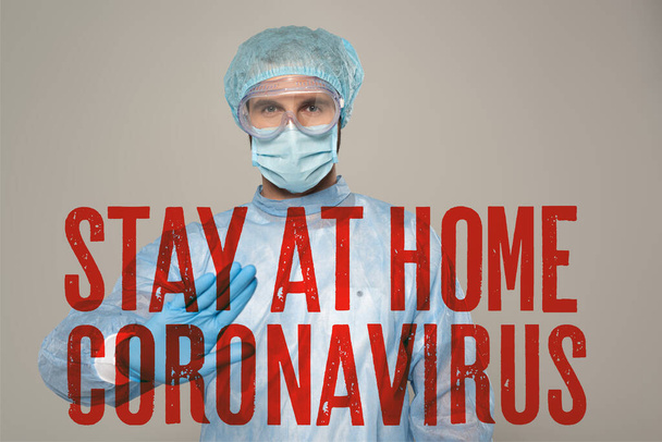Врач в медицинской маске показывает стоп-жест на камеру, изолированную на сером, оставайтесь дома и коронавирусную иллюстрацию
 - Фото, изображение