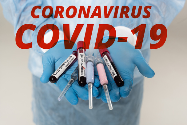 Vista recortada del médico sosteniendo tubos de ensayo con muestras de sangre y letras de coronavirus y jeringas aisladas en gris, ilustración del coronavirus covid-19
 - Foto, Imagen