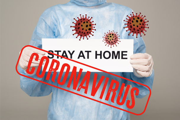 Cropped view of doctor in latex gloves holding card with stay at home lettering isolated on grey, coronavirus and bacteria illustration - Photo, Image