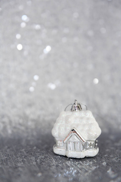 Christmas, New Year background and texture. Christmas tree toy house in the snow, stands on a material or fabric embroidered with glaring silver sequins - Zdjęcie, obraz