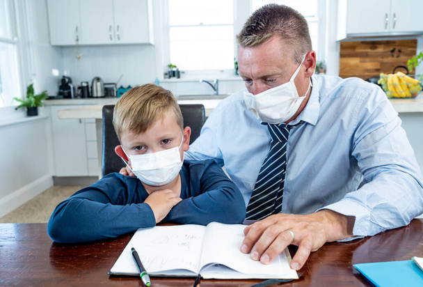 Coronavirus Outbreak school shutdowns. Stressed parent coping with remote work and homeschooling worried about COVID-19 pandemic. Father and son with mask in quarantine working and learning from home. - Foto, Bild