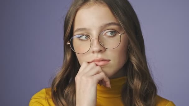 A close-up view of calm girl in eyeglasses is thinking about something isolated over a purple background in studio - Materiał filmowy, wideo