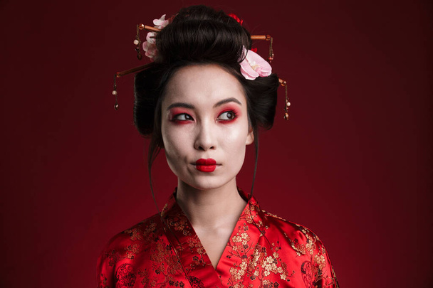 Image of attractive asian geisha woman in traditional japanese kimono isolated over red background - Zdjęcie, obraz