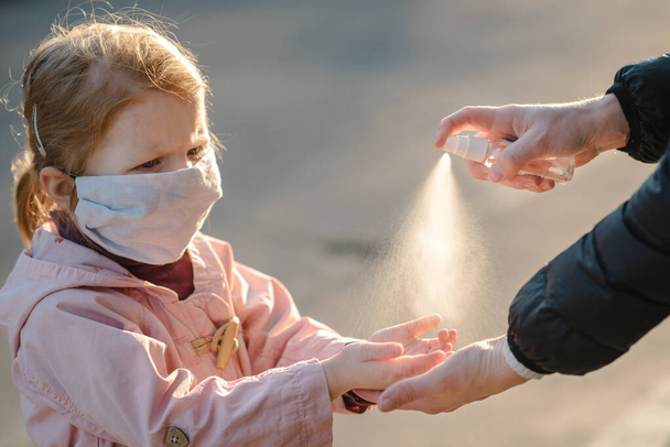 Coronavirus. Woman use spray sanitizer on hands child in a protective mask on the street. Preventive measures against Covid-19 infection. antibacterial hand-washing spray. Illness protection. - 写真・画像