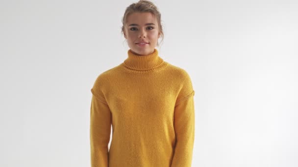 Happy pretty blonde woman in sweater posing and looking at the camera over grey background - Filmmaterial, Video