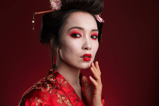 Bild der attraktiven asiatischen Geisha-Frau im traditionellen japanischen Kimono isoliert über rotem Hintergrund - Foto, Bild