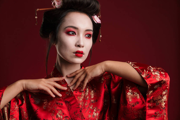 Image of attractive asian geisha woman in traditional japanese kimono isolated over red background - Photo, image