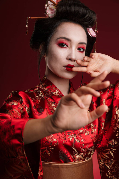 Image of young asian geisha woman in traditional japanese kimono dancing isolated over red background - Foto, immagini