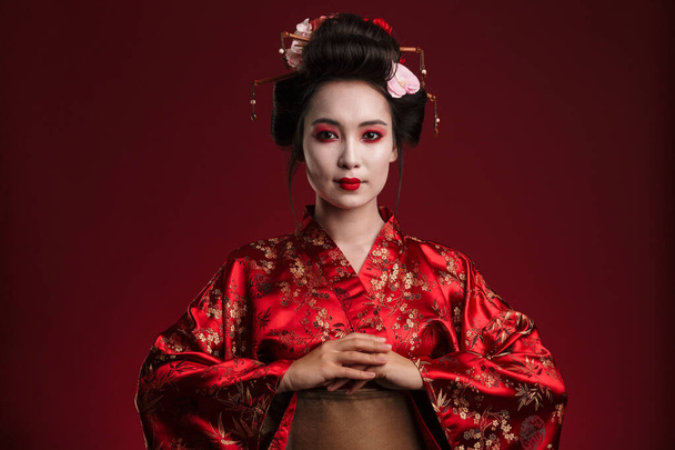 Image of beautiful young geisha woman in traditional japanese kimono isolated over red background - Фото, зображення