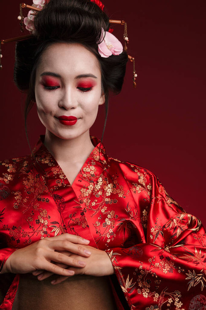 Image of beautiful young geisha woman in traditional japanese kimono isolated over red background - Valokuva, kuva