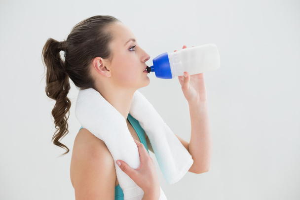 Fit woman with water bottle against wall - Foto, Imagen