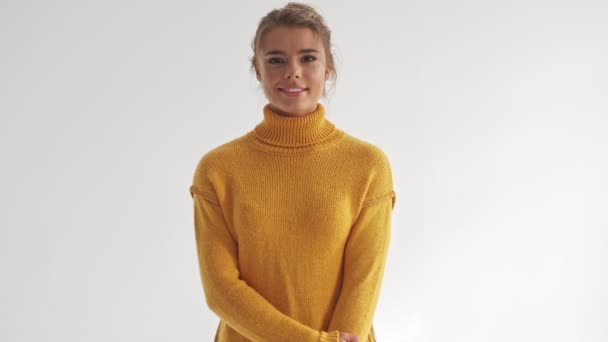 Pleased pretty blonde woman in sweater posing and looking at the camera over grey background - Video