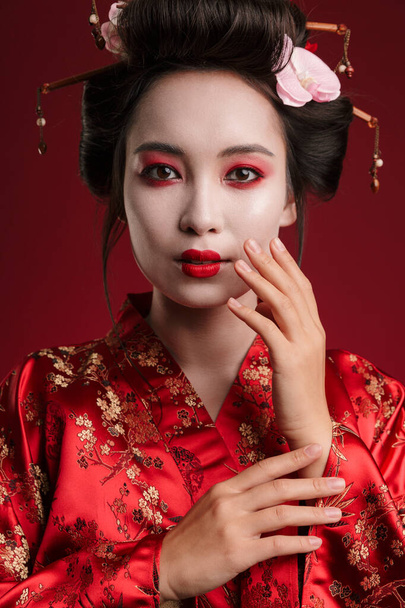 Image of charming geisha woman in traditional japanese kimono dancing isolated over red background - Photo, Image