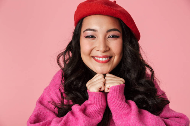 Image of young beautiful asian girl wearing beret smiling and clenching her fists at chest isolated over pink background - 写真・画像