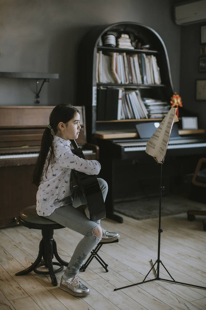Söpö pieni tyttö harjoitellaan akustinen kitara maalaismainen koti - Valokuva, kuva
