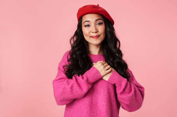 Image of young beautiful asian girl wearing beret smiling and holding her hands at heart isolated over pink background - Fotografie, Obrázek