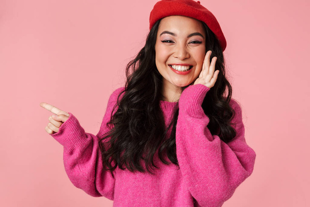Image of young beautiful asian girl wearing beret laughing and pointing finger at copyspace isolated over pink background - Fotografie, Obrázek