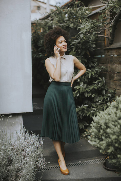 Elinde cep telefonu olan güzel kıvırcık saçlı kadın arka bahçede duruyor. - Fotoğraf, Görsel