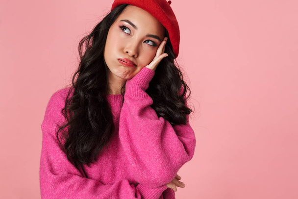 Image of bored beautiful asian girl with long dark hair wearing beret looking at copyspace isolated over pink background - 写真・画像