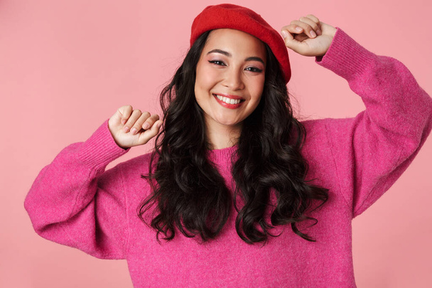Image of young beautiful asian girl wearing beret rejoicing and smiling at camera isolated over pink background - Photo, image