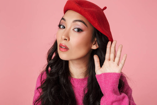 Image of confused asian girl trying to hear while keeping hand at her ear isolated over pink background - Fotoğraf, Görsel