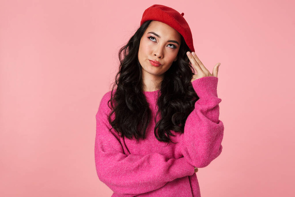 Image of serious beautiful asian girl wearing beret gesturing gun fingers at his temple isolated over pink background - Photo, Image