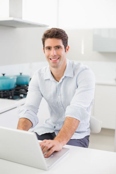 Smiling man using laptop at home - Фото, изображение