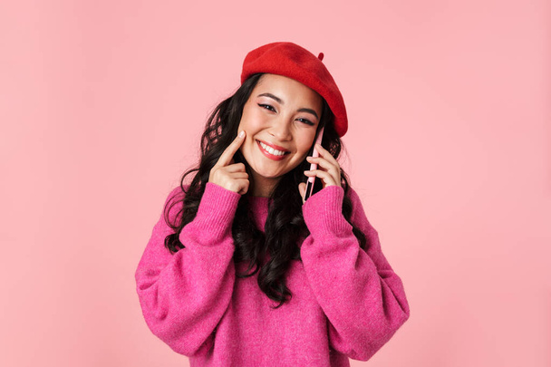 Image of attractive beautiful asian girl wearing beret smiling and talking on smartphone isolated over pink background - Φωτογραφία, εικόνα