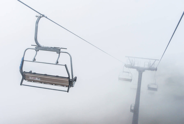 Prázdná křesla otevřené lanovky v horách na pozadí husté mlhy a mraků - Fotografie, Obrázek