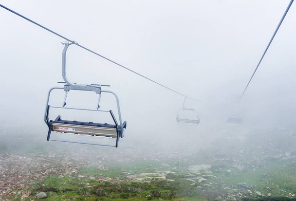 Prázdná křesla otevřené lanovky v horách na pozadí husté mlhy a mraků - Fotografie, Obrázek