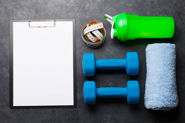 Fitness vybavení a prázdný list pro cvičení plán na dřevěném pozadí. Horní pohled plochý ležel s kopírovacím prostorem - Fotografie, Obrázek
