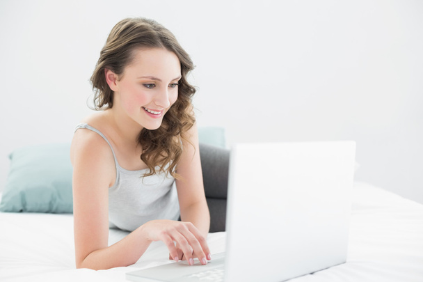 Smiling casual brunette using laptop in bed - Foto, imagen